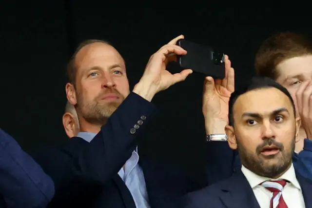 Prince William pictured in the Istanbul stadium holding his phone up taking a picture