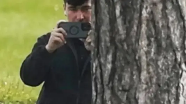 Man behind tree films on iPhone.