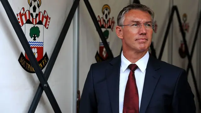 Nigel Adkins in a suit stood in front of the Southampton crest.