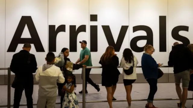 People wait to greet friends and relatives in front of a huge sign reading "Arrivals" at Heathrow Airport.