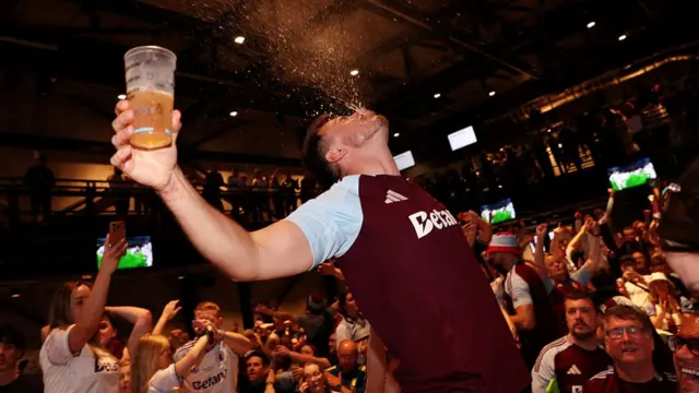 A Villa fan sprays beer in the air as others celebrate in the background