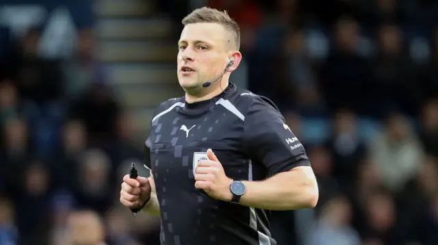 Referee Josh Smith in black kit refereeing the play-off semi-final second leg between Stockport and Stevenage
