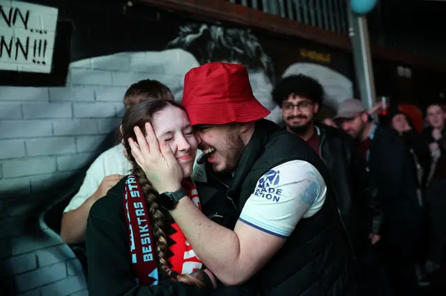 Two Aston Villa fans celebrate, a man is holding a woman's face
