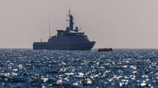A French Warship escorts an inflatable 'small boat' carrying migrants across the channel.