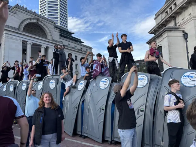 Villa fans climb on the top of Portaloos to stand up and get a glimpse of the victory bus.