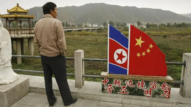 Backview of a man standing next to a monument featuring the North Korea and China flags