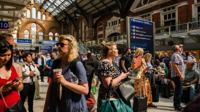 Travelers wait at Liverpool Street railway station during hot weather