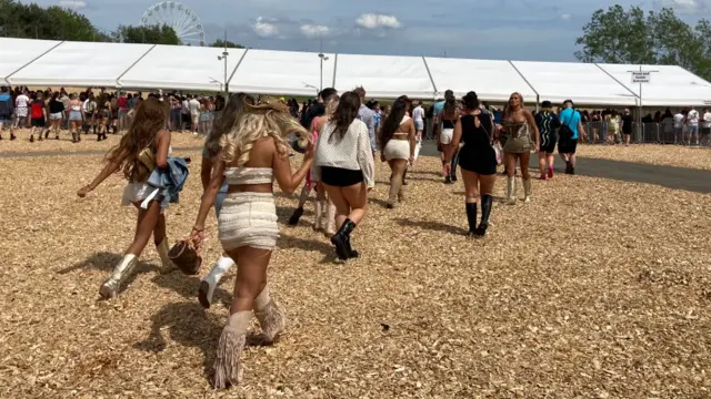 Festival-goers dressed in boots walk across the grounds.