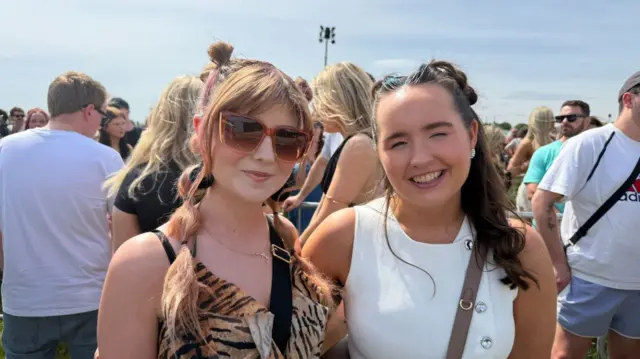 Two women hugging and smiling at the camera in line for the festival
