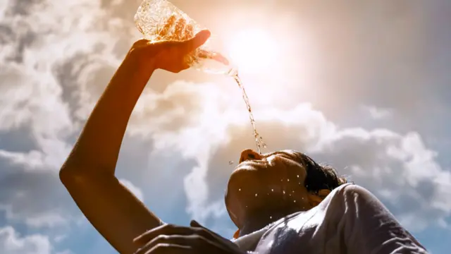 Young woman drinking fresh water from a plastic bottle under the hot summer sun