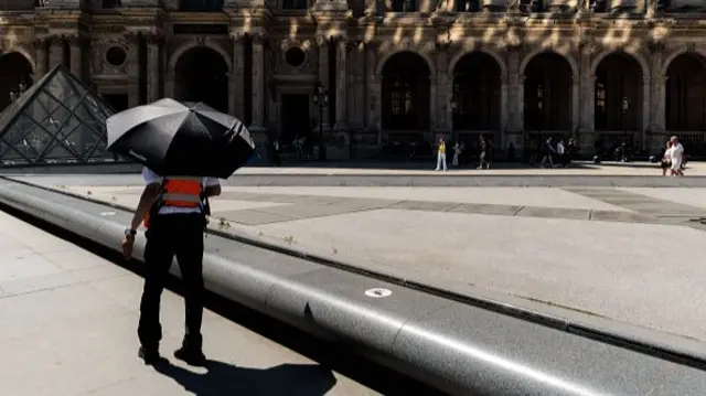 A security guard at the Louvre in Paris takes shelter under an umbrella