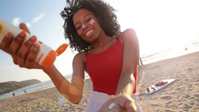 Young woman squeezes sunscreen on beach.