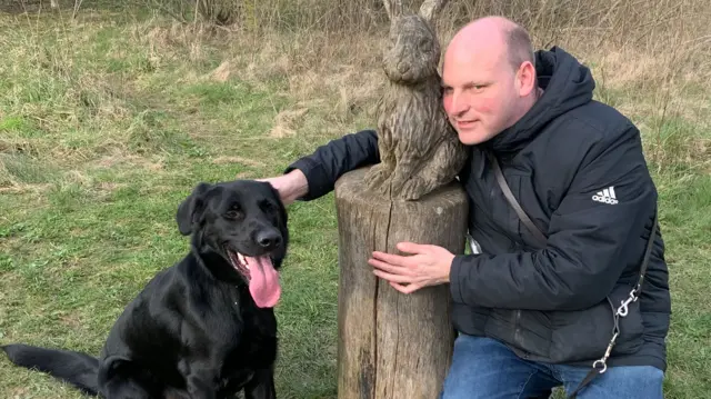 Sean pets his guide dog next to a statue of a rabbit.