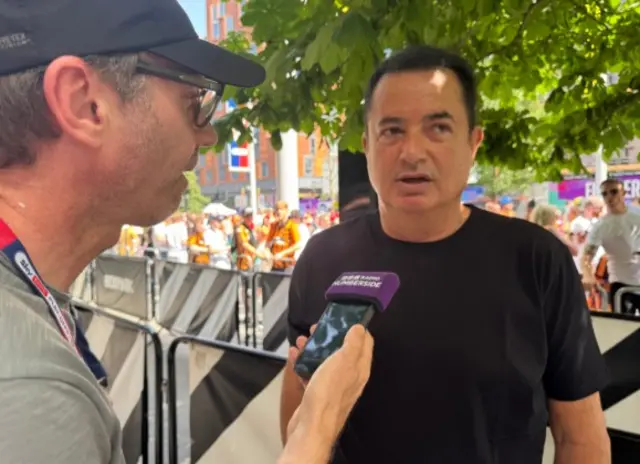 The owner stands to the left of the picture in a black t-shirt.  Matt wears a grey shit and holds a phone up as he is doing thecinterview.