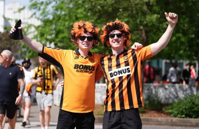 Two Hull fans wearing orange and black wigs. The fan on the left is wearing a mainly orange Hull shirt and the one on the right is wearing a shirt with orange and black vertical stripes