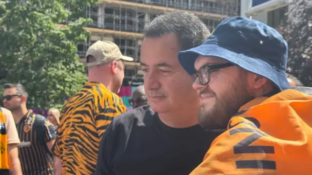 A Hull City fan, with a black and amber flag draped over his shoulders, poses for a selfie with club owner Acun Ilicali