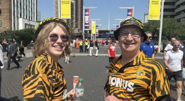 Melissa stands on the left in an orange and black tiger top and matching hat.  Her father wears a Tigers bucket hat and Hull City shirt.