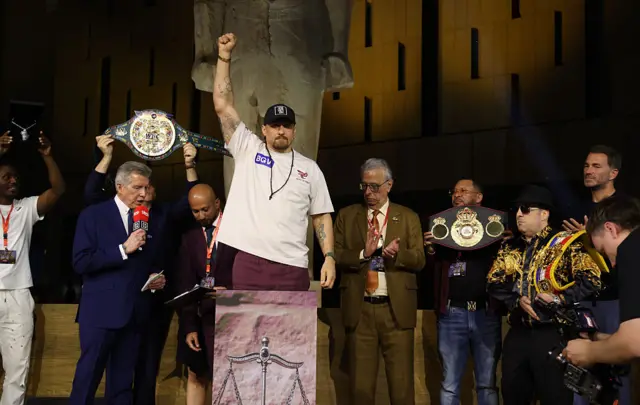 Oleksandr Usyk standing with his hand in the air on the scales