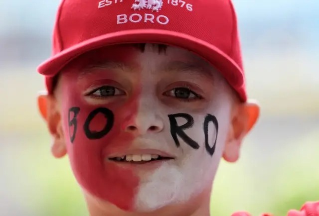 A young Boro fan wearing a red Middlesbrough cap with his face painted red on one side and white on the other side and the word Boro in black across his face