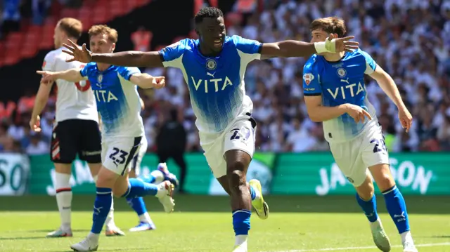 Adama Sidibeh celebrates scoring with his arms stretched out