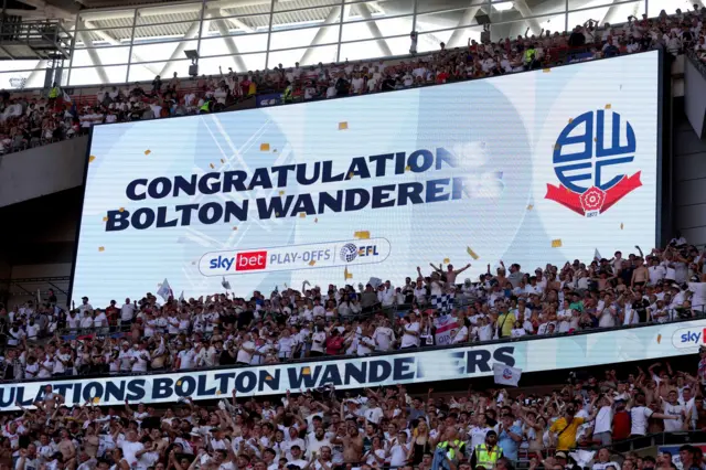 Bolton fans celebrate in front of a screen that says "Congratulations Bolton Wanderers" at Wembley