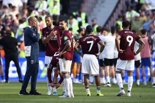 West Ham players and staff stand desconsolate on the pitch