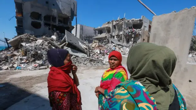 Three women gathered near the sit of a strike in southern Lebanon. Rubble of buildings can be seen behind them