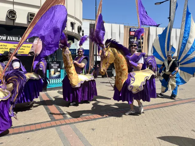 Men in purple costumes on gold horse models.