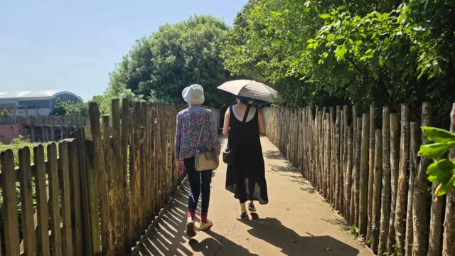 Two women walking in Colden Common, Hampshire, with one wearing a sun hat and the other holding an umbrella for shade
