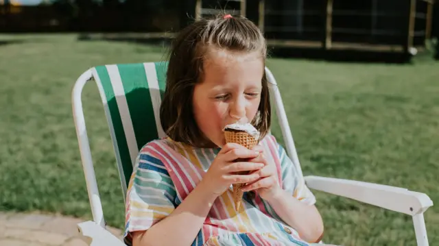 Girl sits in deck chair eating ice cream