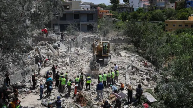Rescue workers looking on at the rubble-filled site of buildings after they have been hit by Israeli strikes