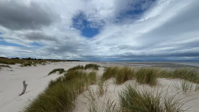 Cloudy conditions with small pockets of blue sky peeking through in Nairn, Highlands, with beach scene and grasses in foreground