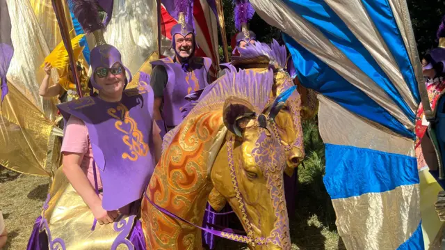 Men dressed in purple outfits on gold horse models