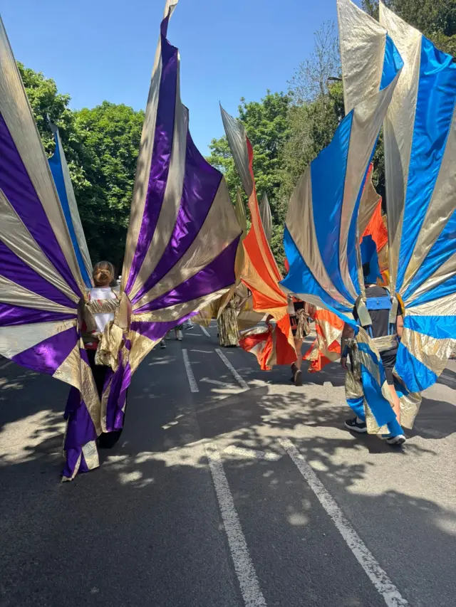 High-winged costumes, with people walking along a street.