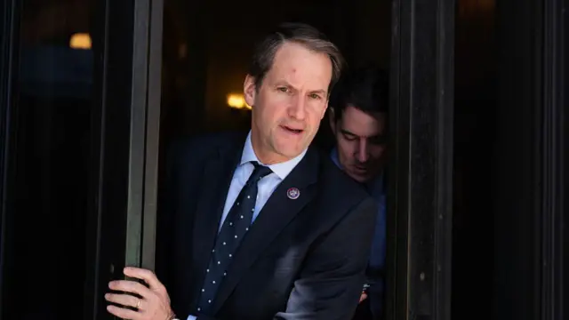 Congressman Jim Himes in a dark suit as he walks out past revolving doors of a building