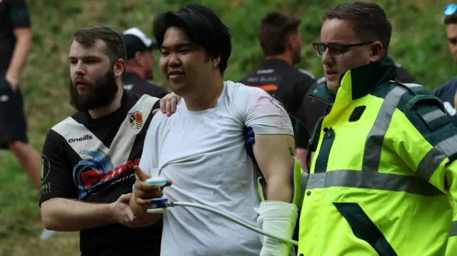 A man being escorted from Cooper's Hill with an injured arm
