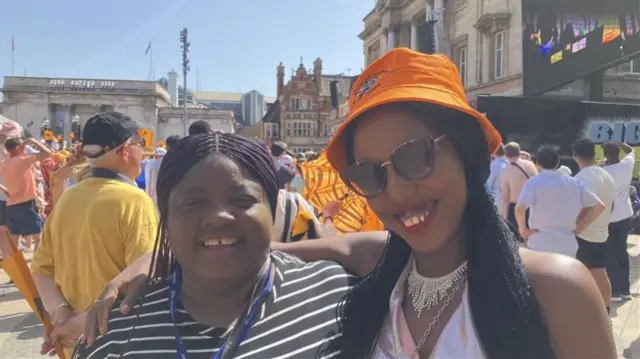 Two women, one wearing a Hull City amber bucket hat, smile and embrace as they have their photo taken.