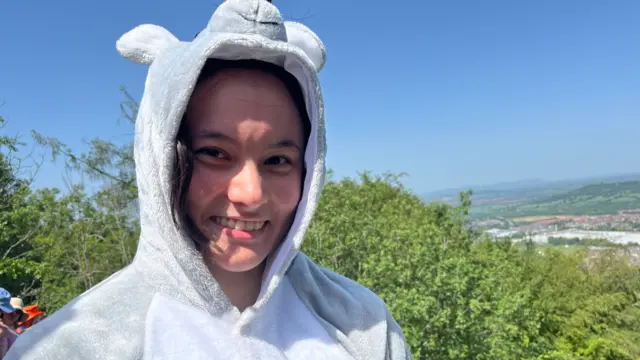 A woman dressed in a mouse onesie. She is looking ahead and smiling.