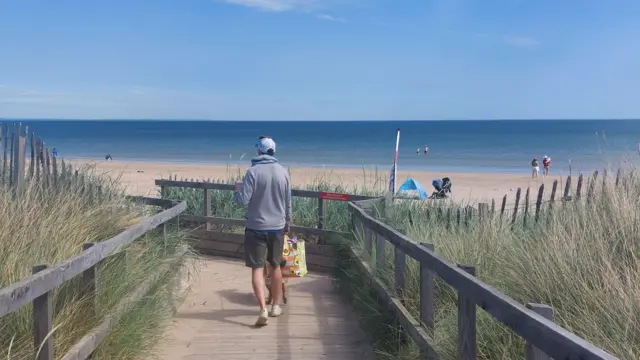 A man walks on a boardwalk to a beach in St Andrews, Fife.