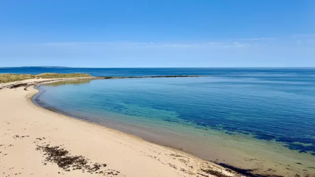 An unoccupied beach in Northumberland with yellow sand and blue-green sea