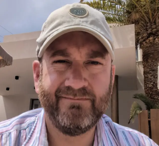 A bearded man in a cap and striped shirt.