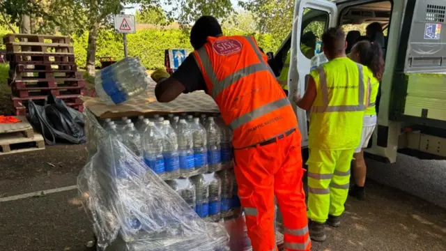 Men unpack crates of bottled water from a white van