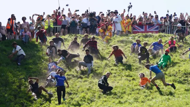 Men are rolling down a green hill at the first cheese race of the day