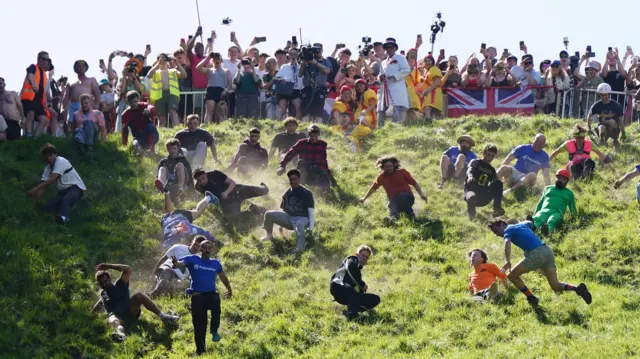 A picture of the cheese rolling - people fly down a very steep hill as spectators watch on