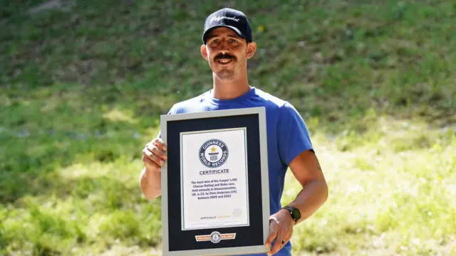 A man wearing a hat and a blue t shirt is holding a large framed certificate.
