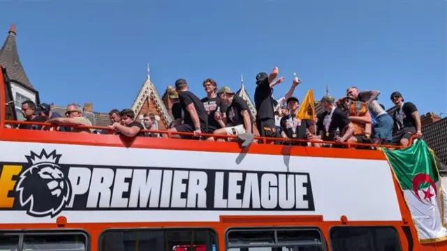 A close up of the players on the top of the open bus, some raise their drinks to cheer, others stand and laugh as the bus proceeds.