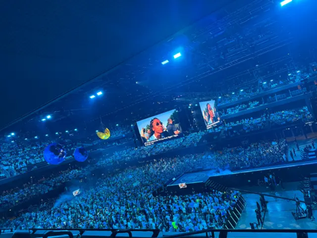 Large crowd of fans inside the Co-Op Live in Manchester. They are all illuminated in sky blue, the club colours of Manchester City