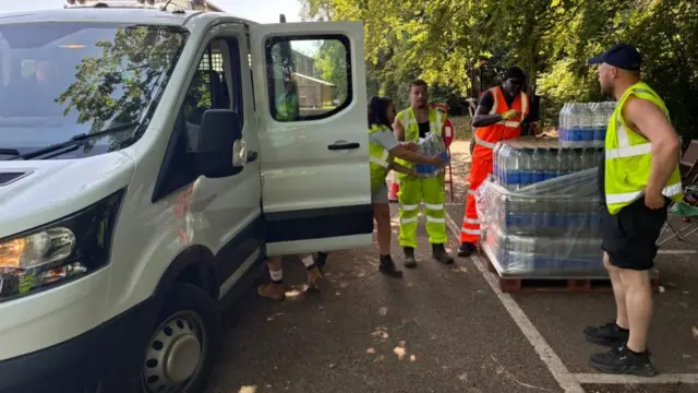Men unload crates of bottled water from a white van