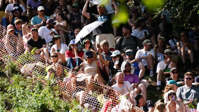 People are sitting on the side of a hill wearing hats and sunglasses.