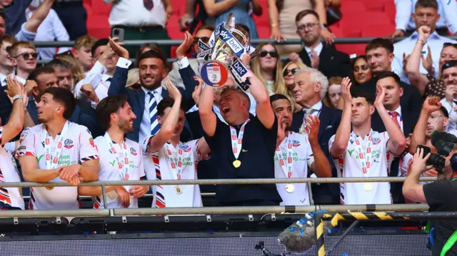 Bolton boss Steven Schumacher lifts the play-off trophy with his team